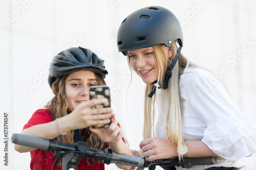 Teenager girls using mobile application to unlock and rent riding public rental electric scooters in urban city environment. Eco-friendly modern public city transport in Ljubljana, Slovenia.