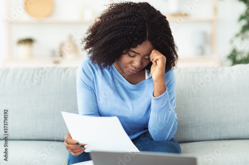 Sad black woman holding papers sitting with laptop