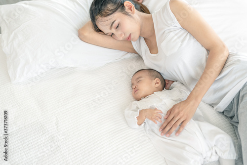 Top view of beautiful young Asian mom and her cute little baby sleeping in bed at home.