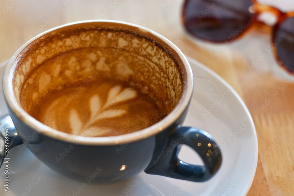 Close-up view cappuccino, Drinking hot coffee in a blue cup with sunglasses background. Close-up view cappuccino, Drinking hot coffee in a blue cup with sunglasses background.