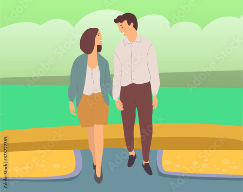 Couple walking down the street. Young guy and girl holding hands, looking at each other, walking in summer day in city park, romantic walk. Pleasant promenade in open air on a date, active lifestyle