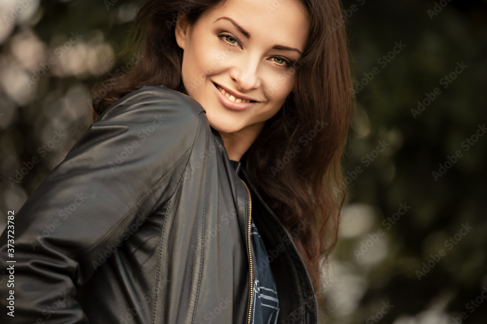 Beautiful brunette smiling business successful woman enjoying in leather black jacket doing active joyful moving on summer day trees colors. Closeup Beautiful brunette smiling business successful woman enjoying in leather black jacket doing active joyful moving on summer day trees colors. Closeup