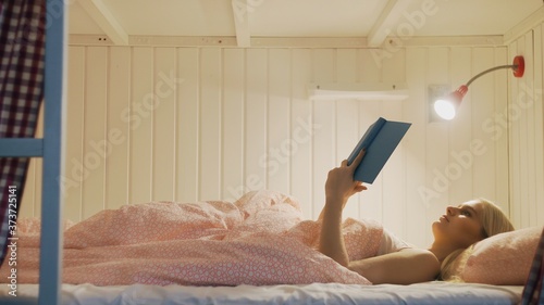 Woman in night underwear finished read book, turns light off and goes to sleep in cozy hostel room