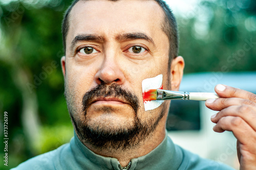 A man paints a revolutionary opposition white and red flag on his cheek with a brush in protest against the dictatorial regime in Belarus. Elections of the Belarusian president. Strikes of the people