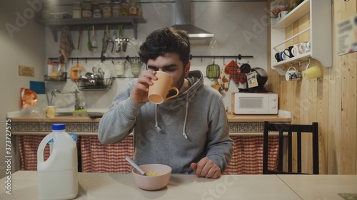 A young man having breakfast in the kitchen. Man eats Corn Flakes Cereal and drinks a coffee