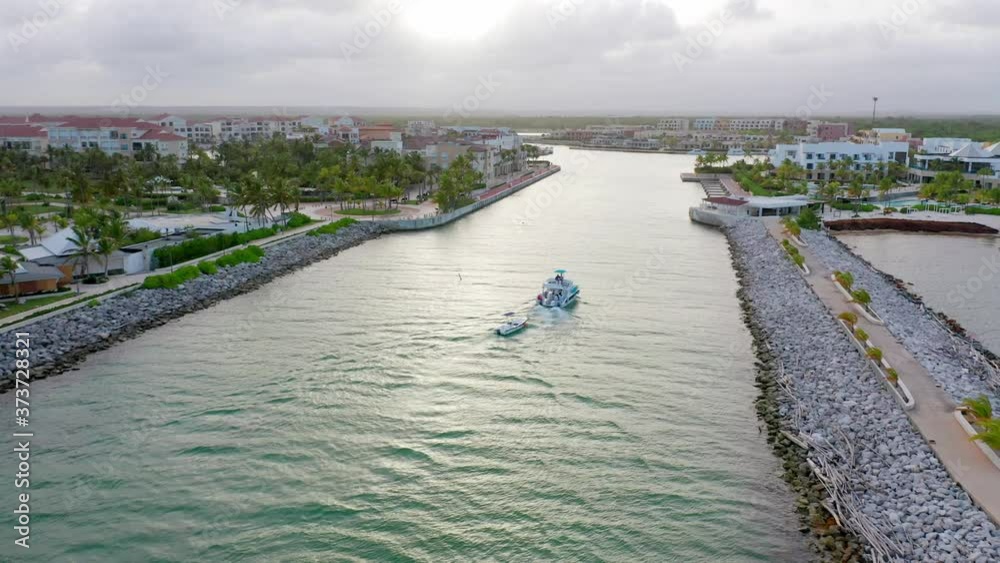 custom made wallpaper toronto digitalFlying Behind a White Luxury Yacht Traveling in Towards the Cap Cana Marina, with Glamorous Hotels and Homes Either Side, Towing a small Dinghy Through Rock Lined Waterway