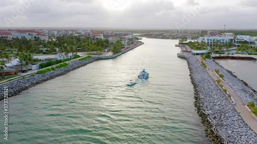 Wallpaper Mural Flying Behind a White Luxury Yacht Traveling in Towards the Cap Cana Marina, with Glamorous Hotels and Homes Either Side, Towing a small Dinghy Through Rock Lined Waterway Torontodigital.ca
