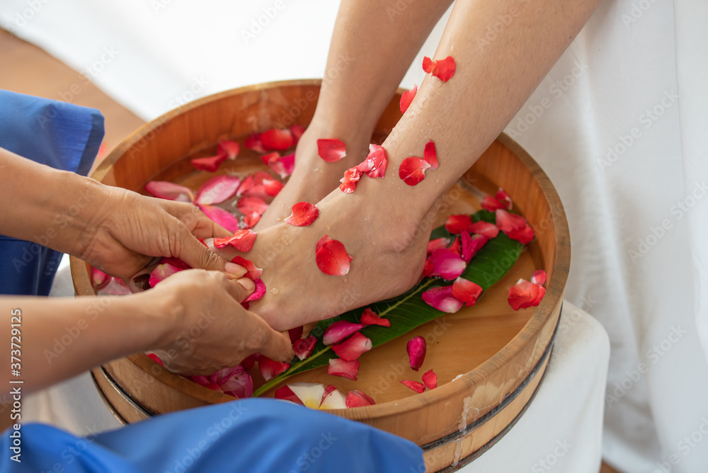 Female feet in wooden bowl with flowers at spa salon Female feet in wooden bowl with flowers at spa salon