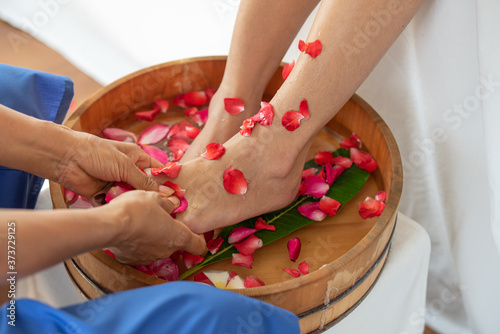 Female feet in wooden bowl with flowers at spa salon