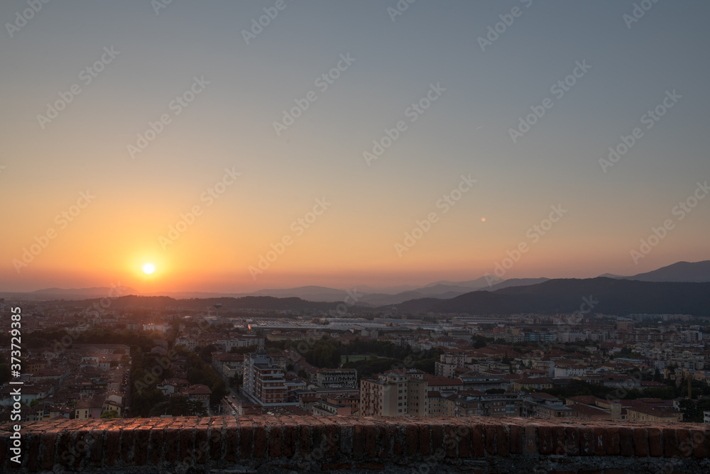 Aerial panoramic sunset view of residential district with buildings of Brescia city and Alps mountain range, blue cloudy sky background, Lombardy, Italy. Brescia Castle.