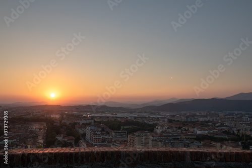 Aerial panoramic sunset view of residential district with buildings of Brescia city and Alps mountain range, blue cloudy sky background, Lombardy, Italy. Brescia Castle.