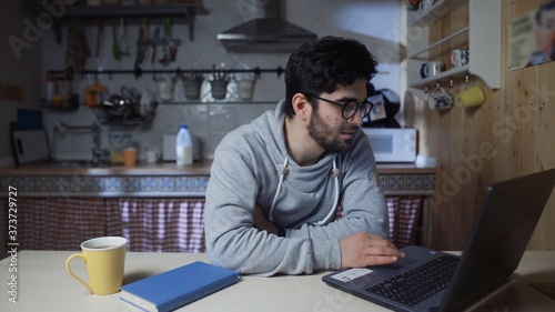 Happy young businessman working on laptop in kitchen at home at night