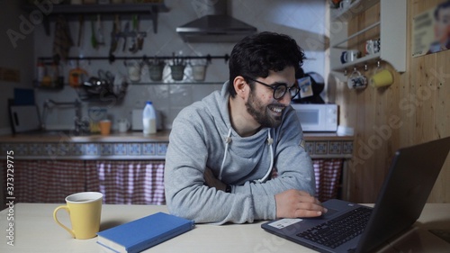 Happy young businessman working on laptop in kitchen at home at night
