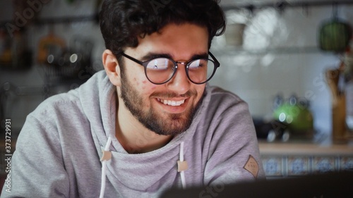 Close up of happy man working on laptop in kitchen at home at night