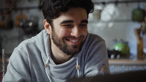 Close up of happy man working on laptop in kitchen at home at night