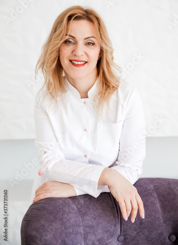 Beautiful young woman doctor posing in a white coat against a white wall background