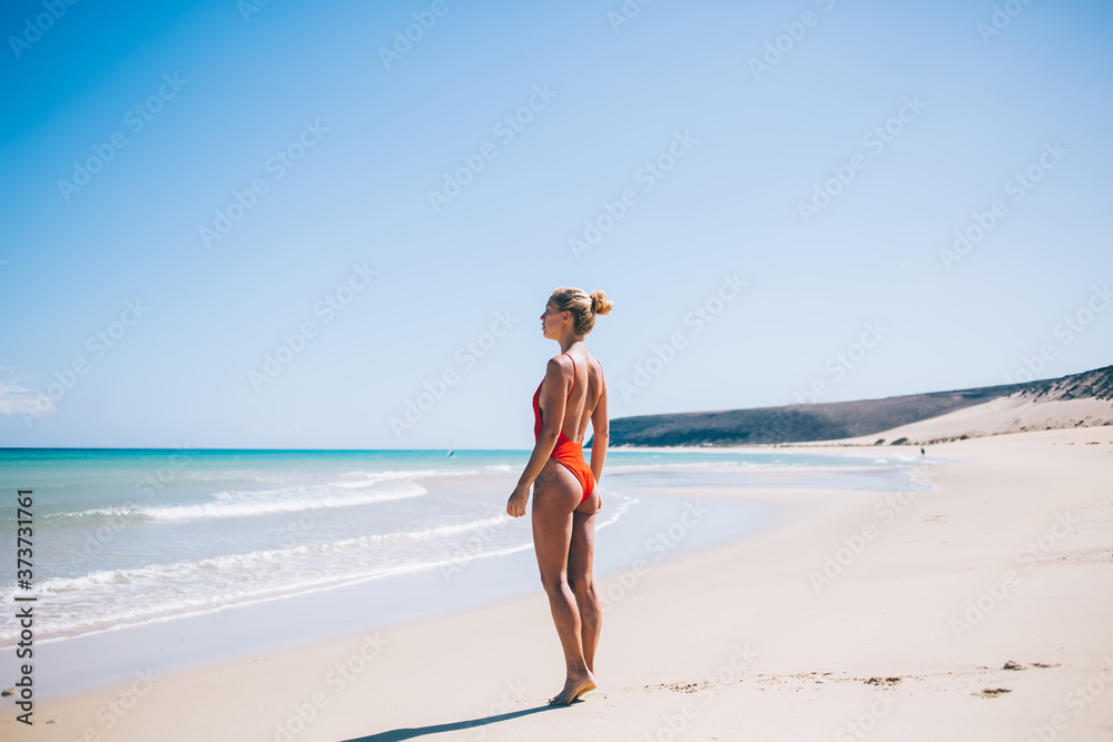 Young female wanderer looking at picturesque seascape during sunbathing at sandy Maldives beach, travel woman enjoying paradise recreation during summer vacations on Balearic islands in Spain