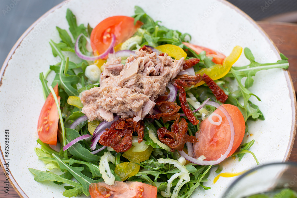 White plate with delicious vegetable tuna salad with sun-dried tomatoes, arugula on a brown table top view, healthy lifestyle. Bright healthy lunch. Idea of diet recipe. Selective focus, close-up