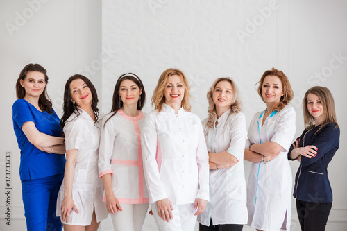 Beautiful young female doctors in white uniforms posing against the background of a white wall.