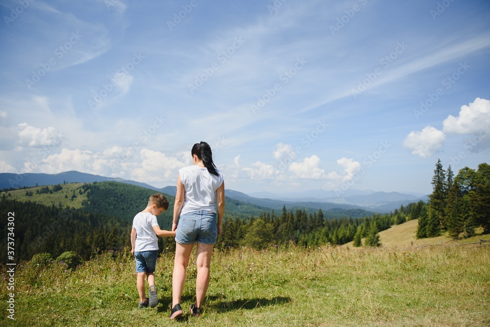 The boy and his mother are standing on the top of the mountain. A woman is traveling with child. Boy with his mother looking at the mountains. Travel with backpacks. Hike and climb with kids. The boy and his mother are standing on the top of the mountain. A woman is traveling with child. Boy with his mother looking at the mountains. Travel with backpacks. Hike and climb with kids.