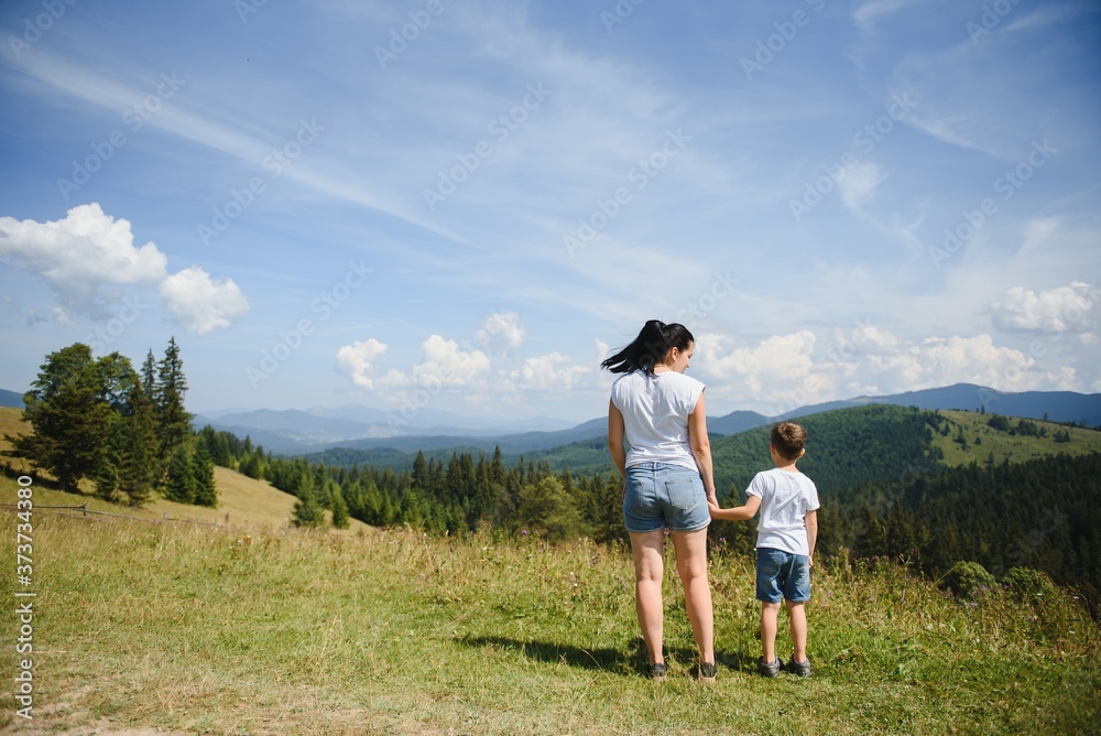 The boy and his mother are standing on the top of the mountain. A woman is traveling with child. Boy with his mother looking at the mountains. Travel with backpacks. Hike and climb with kids.