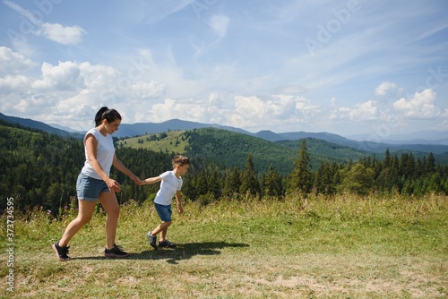 The boy and his mother are standing on the top of the mountain. A woman is traveling with child. Boy with his mother looking at the mountains. Travel with backpacks. Hike and climb with kids. © Serhii