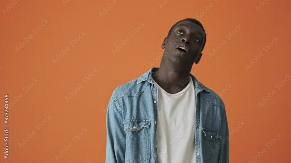 A bored african american young man is looking to the camera standing isolated over an orange background A bored african american young man is looking to the camera standing isolated over an orange background