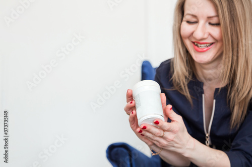 Smiling beautiful woman is looking at remedy in hand while using it for health and beauty
