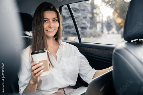 Smart business woman drink coffee and working on her laptop at the back sit of car.