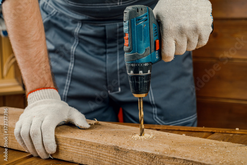 A man in gloves drills a wooden Board