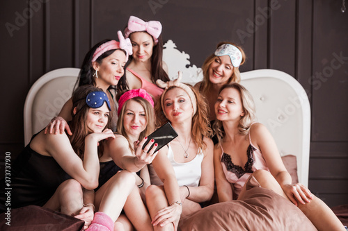 Stylish, trendy, cheerful girls in pajamas and with cosmetic headbands threw a pajama party. Girls are photographed together on the phone
