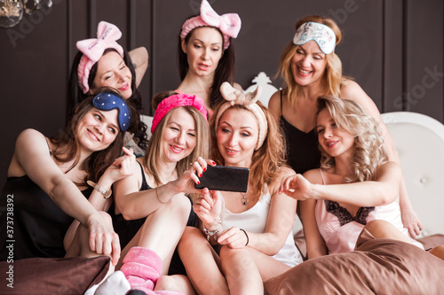 Many girlfriends girls threw a pajama party on a plush bed. Girls smile, look at the camera and take a selfie