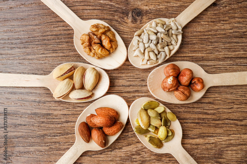 Some of the assorted nuts with pistachios, almonds, pumpkin seeds, sunflower seeds, hazelnuts in wooden spoons on a wooden background, top view.close-up Some of the assorted nuts with pistachios, almonds, pumpkin seeds, sunflower seeds, hazelnuts in wooden spoons on a wooden background, top view.close-up