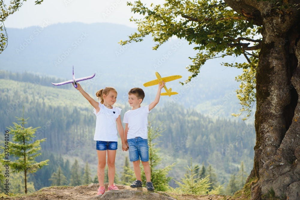 Boy and girl playing with toy airplanes on a background of mountains. Happy childhood and vacation in the mountains.
