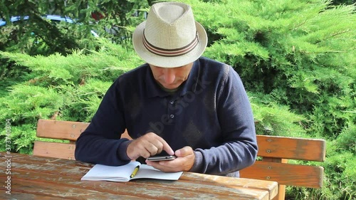 Middle Age Man Transcribing Something From Notebook to His Smartphone