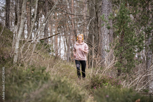 Active sporty woman listening to the music while running in autumn fall forest. Female runner training outdoor. Healthy lifestyle image of young caucasian woman jogging outside. © kasto