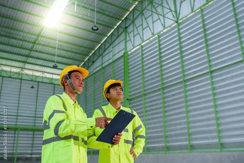Two young Asian workers Wear safety clothing and helmet. Jointly think and work on construction design on the construction site Two young Asian workers Wear safety clothing and helmet. Jointly think and work on construction design on the construction site