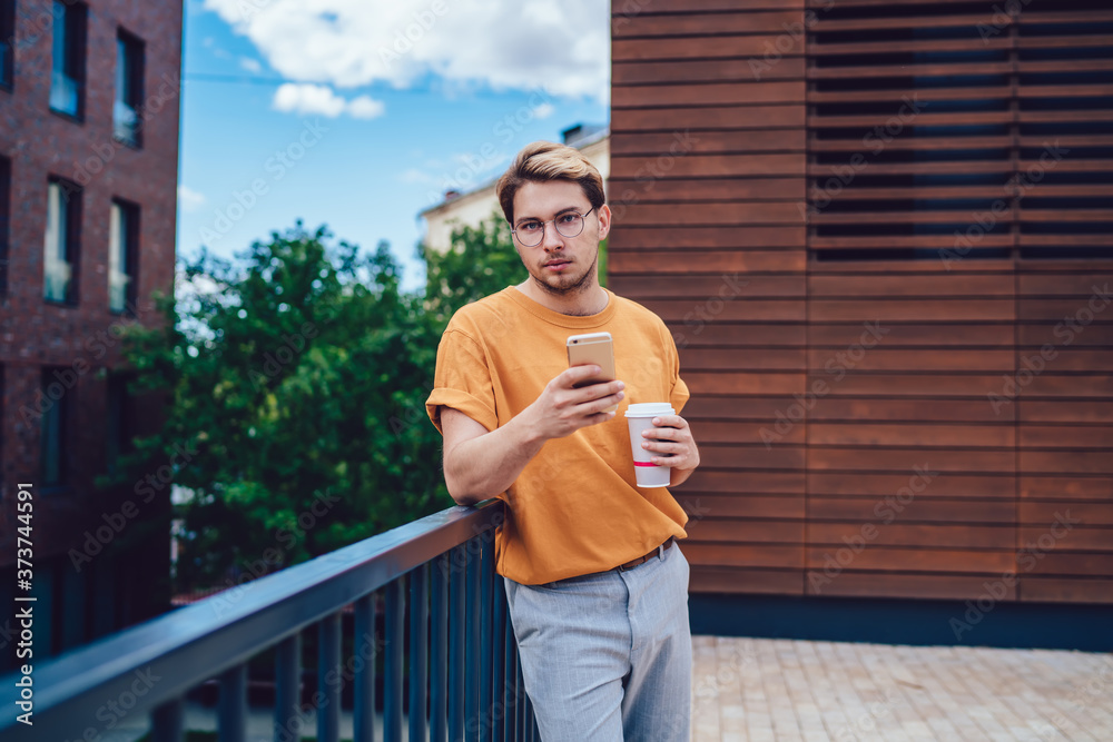 Fototapeta premium Calm male with smartphone and beverage on terrace