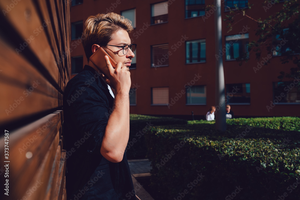 Fototapeta premium Serious student answering phone call near wooden building