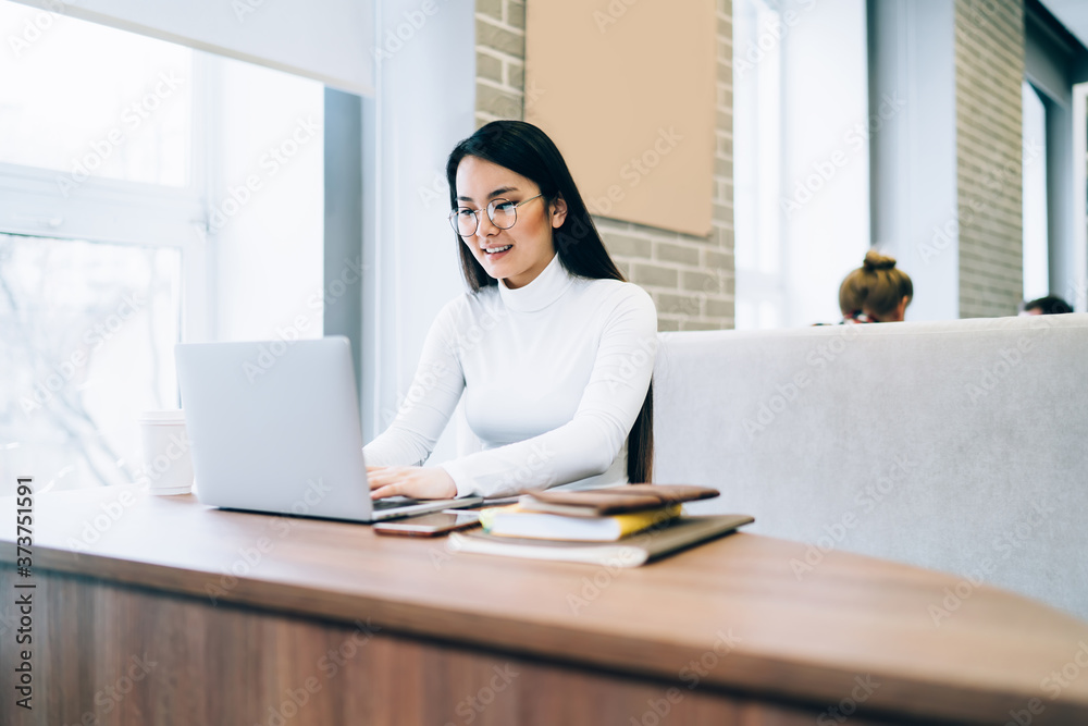 Smiling Asian woman in glasses working on laptop at table Smiling Asian woman in glasses working on laptop at table