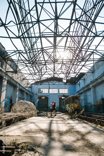 young couple kissing on the background of a large empty building with metal structures
