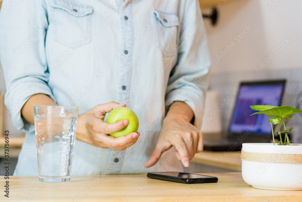 Fototapeta premium Woman drinking water while using her mobile phone, a fruit on the table.