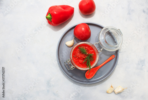 Ajvar  pepper mousse  in a jar and on gray plate and gray backgground. Ajvar - delicious dish of red peppers  tomato and garlic.