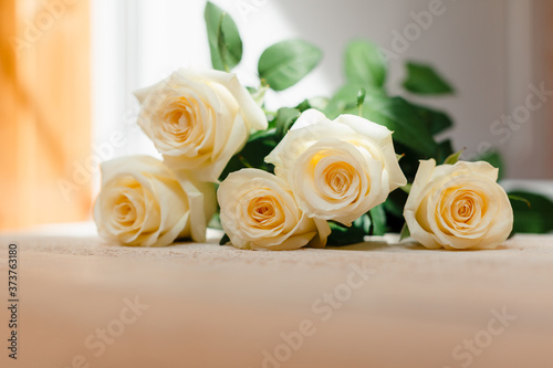 Flowers as a gift for a card, invitation or Wallpaper. 5 white (tea) roses in a bouquet lie on a white wooden table close-up with a blurred background and space for text.