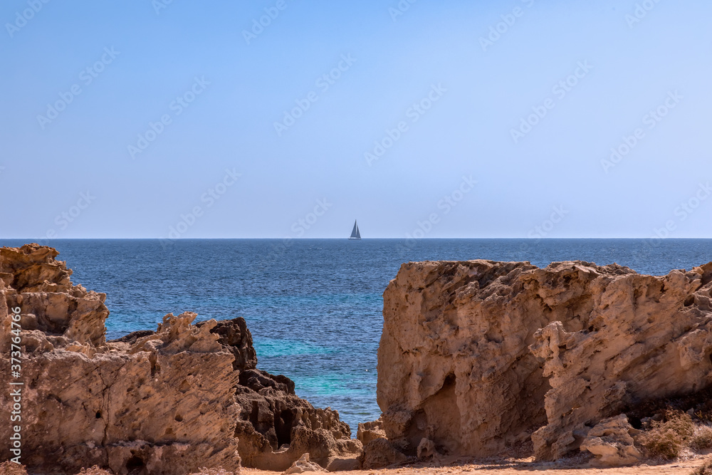 Seascape with lonely sailing yacht at sea and rocky coast of Ibiza island Seascape with lonely sailing yacht at sea and rocky coast of Ibiza island