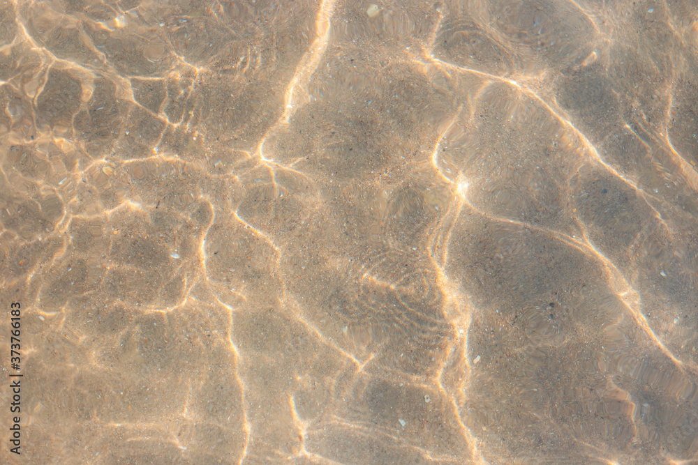 Fototapeta clear sea water with waves and sun reflection on the sandy bottom. Water texture