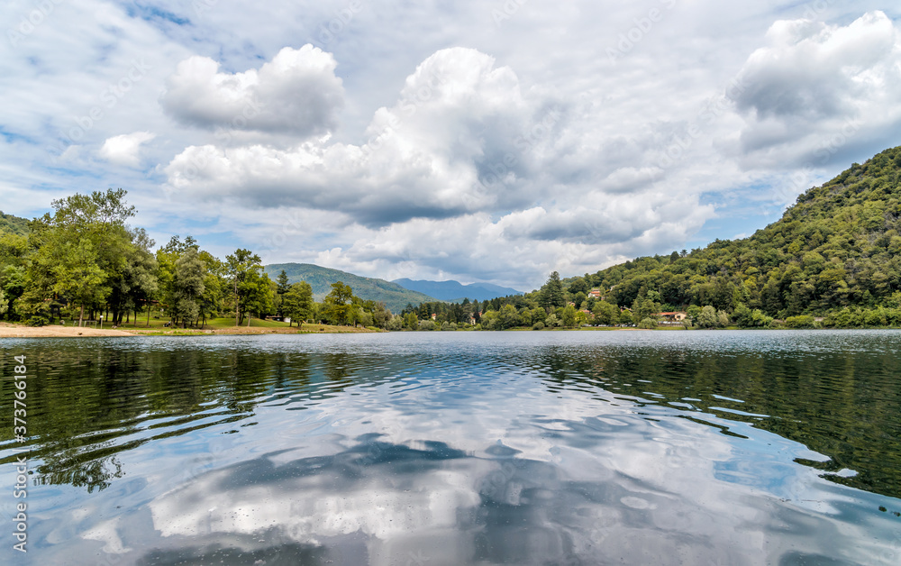 Fototapeta premium Landscape of Lake Ghirla with reflections of the clouds and trees in a summer day, Valganna, province of Varese, Italy