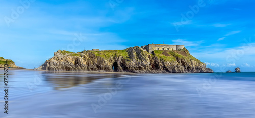 A dreamy long exposure view of the waters edge looking towards Saint Catherine's Island in Tenby, Pembrokeshire at low tide on a sunny day
