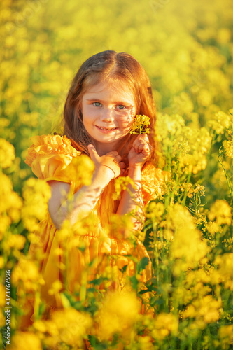 Cute little girl in a yellow dress having fun in the field of flowering canol.