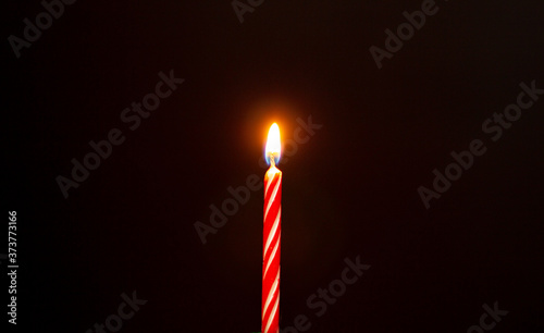 Lights candle. Birthday candle on black background. Red birthday candle.